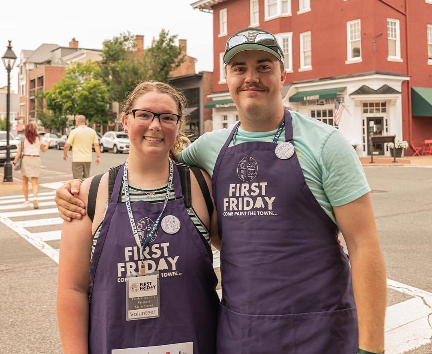 Volunteers in purple First Friday aprons standing on a street corner in Fredericksburg