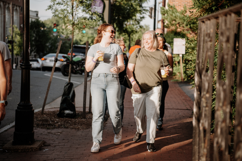 Two women walking in Downtown Fredericksburg drinking orange crushes.